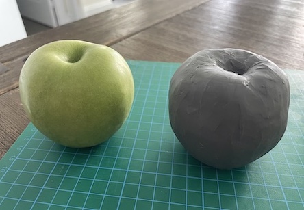 A green apple beside a clay apple